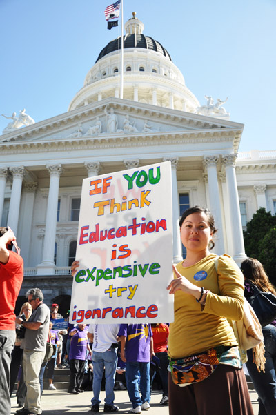 Participant holds sign that reads if you think education is expensive try ignorance